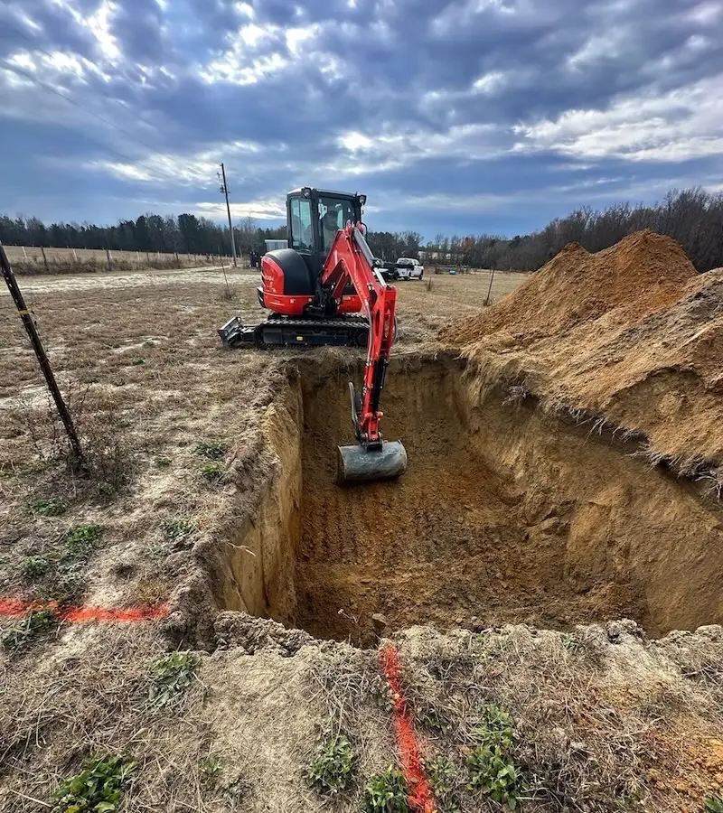 Excavator digging trench on construction site for tank installation.