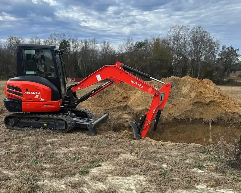 KX040-4 mini excavator digging a large hole in a rural outdoor setting.